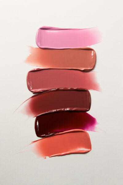 Five smears of different colored lip glosses or paints on a white background, arranged in a vertical line.