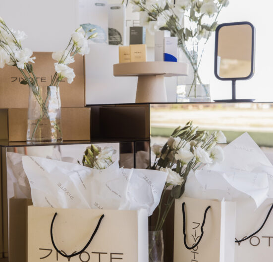 Kozmetički proizvodi s oznakom Divote i korejska kozmetika postavljeni su na stolu, okruženi cvijećem i zrcalom, stvarajući elegantan prikaz.