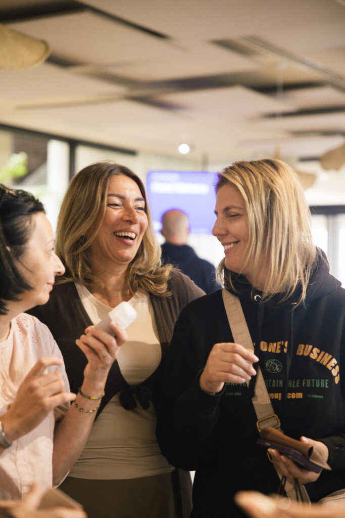 Tri nasmiješene žene drže proizvode od Divote Cosmetics, fokusirane na korejsku kozmetiku, dok razgovaraju u zatvorenom prostoru.