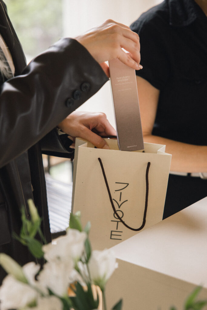 Osoba vadi kutiju s korejskom kozmetikom Haruharu Wonder iz papirnate vrećice s natpisom 'Divote Cosmetics'.