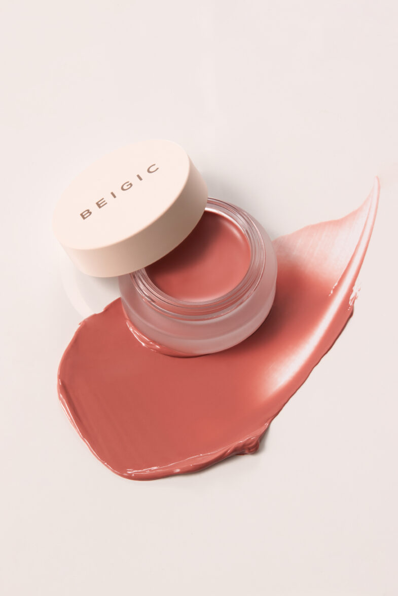 A jar of BEIGIC cream blush with an open lid, surrounded by a smooth smear of pinkish color.