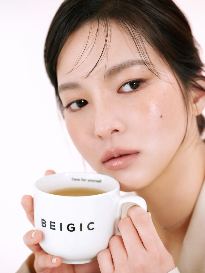 A person holding a cup with "BEIGIC" on it, containing a light-colored beverage, close to their face.