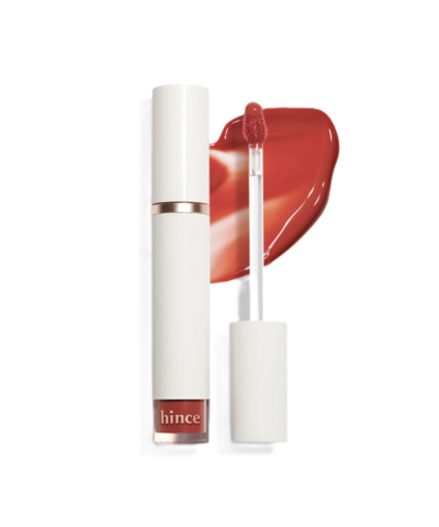 A tube of hince lipstick with a white cap, accompanied by an applicator and a smear of reddish-orange color.