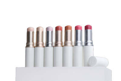 Seven lipsticks in various shades of pink and nude are displayed upright on a white surface against a black background.